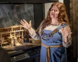 En kvinna i vikingakläder berättar om en modell av en vikingagård på ett vikingamuseum.