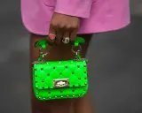 Borsa verde neon, colore complementare del fucsia, con borchie dorate e catena. Indossata da una mano con anelli.