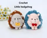 Dos adorables erizos de crochet, uno beige con pajarita amarilla y otro rosa con pajarita roja, posan junto a un ramo de margaritas.
