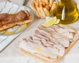 Chicharrón de Cádiz, lonchas de panceta crujiente, limones y palitos de pan, listos para disfrutar.