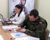 Żołnierz w mundurze stempluje dokumenty, kobieta pracuje przy laptopie. Proces związany z wiekiem poborowym w Polsce.