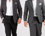 Two men in suits. The one on the left wears a dark grey sport coat with black pants. The one on the right wears a medium grey suit. Both are dressed for a wedding.