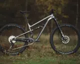 Szary rower górski Polygon Siskiu T8 z pełnym zawieszeniem, gotowy na jesienne trasy po lesie.