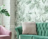 Ein grünes Samtsofa und ein rosafarbener Sessel mit einer Monstera-Pflanze. Die Wand hinter dem Sofa ist mit einer tropischen Tapete mit Palmenblättern dekoriert, eine tolle Idee, um zwei Tapeten zu kombinieren.