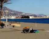 Sonniger fuengirola strand mit Palmen, Bergen und dem Meer im Hintergrund. Kinderwagen und Gepäck liegen am Sand.