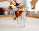 Ręka wylewa espresso na lód w szklance. Idealny napój na upalne dni - tonic espresso.