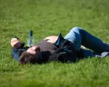Mężczyzna leży na trawie obok butelki wódki. Czy padaczka alkoholowa jest śmiertelna? To pytanie budzi niepokój.