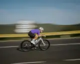 Kolarz w fioletowej koszulce pędzi na rowerze, osiągając prędkość 50 km/h.