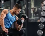 Ein Mann trainiert im Fitnessstudio mit Hanteln. Er fragt sich, wie oft ins Gym pro Woche er gehen sollte, um fit zu bleiben.