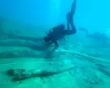 Subacquei esplorano un sito archeologico subacqueo, tra antichi resti di legno. Un'immersione per scoprire cosa vedere.
