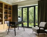 Acogedora habitacion despacho en casa con estanterías de madera, escritorio negro y sillón estampado. Ventanal con vistas al jardín.