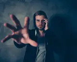 Mężczyzna w kapturze z podbitym okiem sięga ręką, szukając ratunku. Zastanawia się, ile relanium na kaca pomoże mu przetrwać ten koszmar.