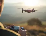 Operator steruje dronem, realizując wideofilmowanie z powietrza. Zachód słońca nad malowniczym krajobrazem.