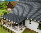 Nowy, ciemnoszary dach z blachodachówki, który przeszedł wymianę dachu, chroni dom i tworzy zadaszenie tarasu.