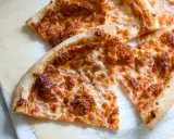 Tranches de pizza au fromage doré, préparées avec un levain rafraichi, sur du papier sulfurisé.