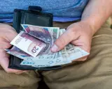 Ręce trzymają portfel z polskimi banknotami. Czy dodatek pielęgnacyjny jest opodatkowany? Pieniądze w portfelu mogą pomóc w odpowiedzi.