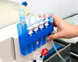 Ręka przygotowuje sprzęt do dializy w domu. Widać aparat, worek z płynem i system przewodów.