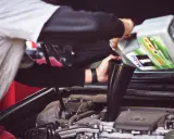 Osoba nalewa olej silnikowy Mobil 1 do silnika samochodu przez lejek.