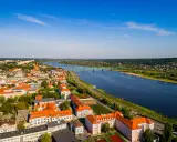 Widok z lotu ptaka na miasto nad Wisłą, z zielonym mostem i zabudowaniami w słoneczny dzień.