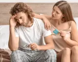 Zmartwiony mężczyzna z prezerwatywą, kobieta z tabletkami. Jak poprawić potencję przy nadciśnieniu?