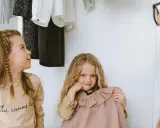 Dwie dziewczynki wybierają ubrania z szafy. Jedna ma warkocz, druga trzyma różową sukienkę.