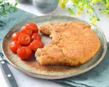 Cotoletta alla milanese dorada y crujiente, acompañada de tomates cherry asados. Un plato clásico y delicioso.