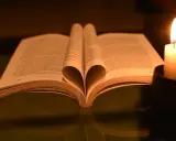 Otwarta księga z kartkami uformowanymi w serce, obok płonąca świeca. W świetle świecy czytam psalm 37 1-4.