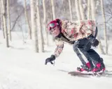 Uśmiechnięta snowboardzistka z różowymi włosami zjeżdża po ośnieżonym stoku wśród drzew. To świetna zabawa podczas chodzenia po górach zimą.