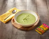 Crema de calabacín para niños, servida en un cuenco blanco sobre tabla de madera. Al lado, un paquete de caldo vegetal Avecrem.