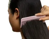 Une main peigne des cheveux noirs et brillants avec un peigne rose. Le peigne est large et espacé, idéal pour démêler les cheveux sans les casser, évitant ainsi les cheveux emmêlés cause.