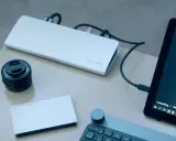 Stacja dokująca ICY BOX podłączona do laptopa, obok obiektyw Sony i dysk Porsche Design.