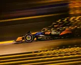 Un coche de **fórmula 1** naranja y negro acelera en la noche, dejando estelas de luz dorada.