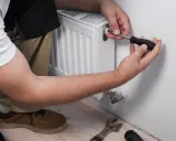 Un técnico usa un destornillador para ajustar la válvula de un radiador, mostrando cómo se abre un radiador para mantenimiento.
