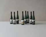 Neun Flaschen Wein der Andreas Oster Weinkellerei stehen nebeneinander.