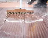 Szczotka z drewnianą rączką czyści brązową deskę kompozytową, tworząc pianę i rozpryskując wodę.
