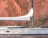 Un voilier Swan 76, avec une voile blanche déployée, navigue près d'une falaise rouge. Un kayak est rangé sur le pont.