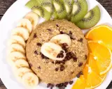 Un délicieux bowl cake flocon d'avoine, garni de rondelles de banane, de tranches de kiwi et d'orange, parsemé de pépites de chocolat.