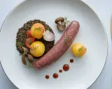 Une saucisse de Toulouse savoureuse, accompagnée de lentilles, de tomates cerises, de champignons et de petites pommes de terre dorées.