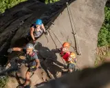 Grupa uśmiechniętych ludzi na via ferracie w Czechach. Wspinają się po skalnej ścianie, zabezpieczeni linami i kaskami.