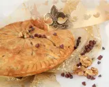 Une galette des rois pépite de chocolat dorée, parsemée de pépites de chocolat et de noix, sous une couronne royale.