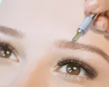 Main d'une esthéticienne réalisant un microblading poil à poil sur un sourcil.