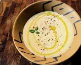 Gazpacho de calabacín cremoso, con un hilo de aceite de oliva, pimentón y una ramita de albahaca, servido en un cuenco artesanal.
