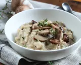 Aksamitne risotto z pieczarkami, udekorowane świeżym tymiankiem, w białej misce na lnianej serwetce.