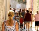 Kobieta z blond kucykiem idzie wąską uliczką pełną ludzi, odkrywając urokliwe villach atrakcje.