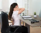 Femme souffrant de douleurs au cou et au dos à son poste de travail. Le travail sédentaire peut causer des problèmes de santé.