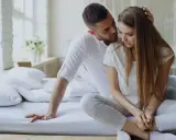 Mężczyzna pociesza smutną kobietę na łóżku. Czy to syndrom sztokholmski?