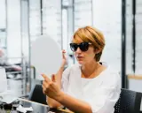 Kobieta w okularach do noszenia na co dzień przymierza nowe okulary w salonie optycznym, patrząc w lusterko.