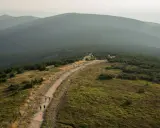 Widok na pasmo górskie Śnieżnik, gdzie szlak prowadzi przez trawiaste zbocza i lasy.