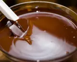 Spatule blanche remuant du chocolat fondu dans un bol en verre. Le chocolat est lisse et brillant, prêt à être utilisé pour une recette.