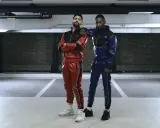 Two gay men in matching red and blue sportswear pose in a parking garage.
